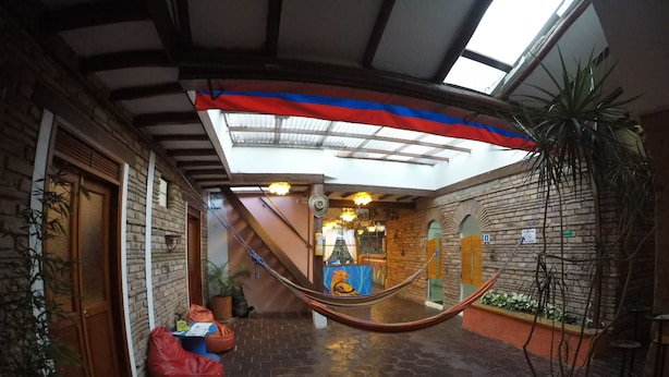 A covered outdoor area with a hammock, potted plants, and a brick wall. - Karuss Hostel (Bogotá)