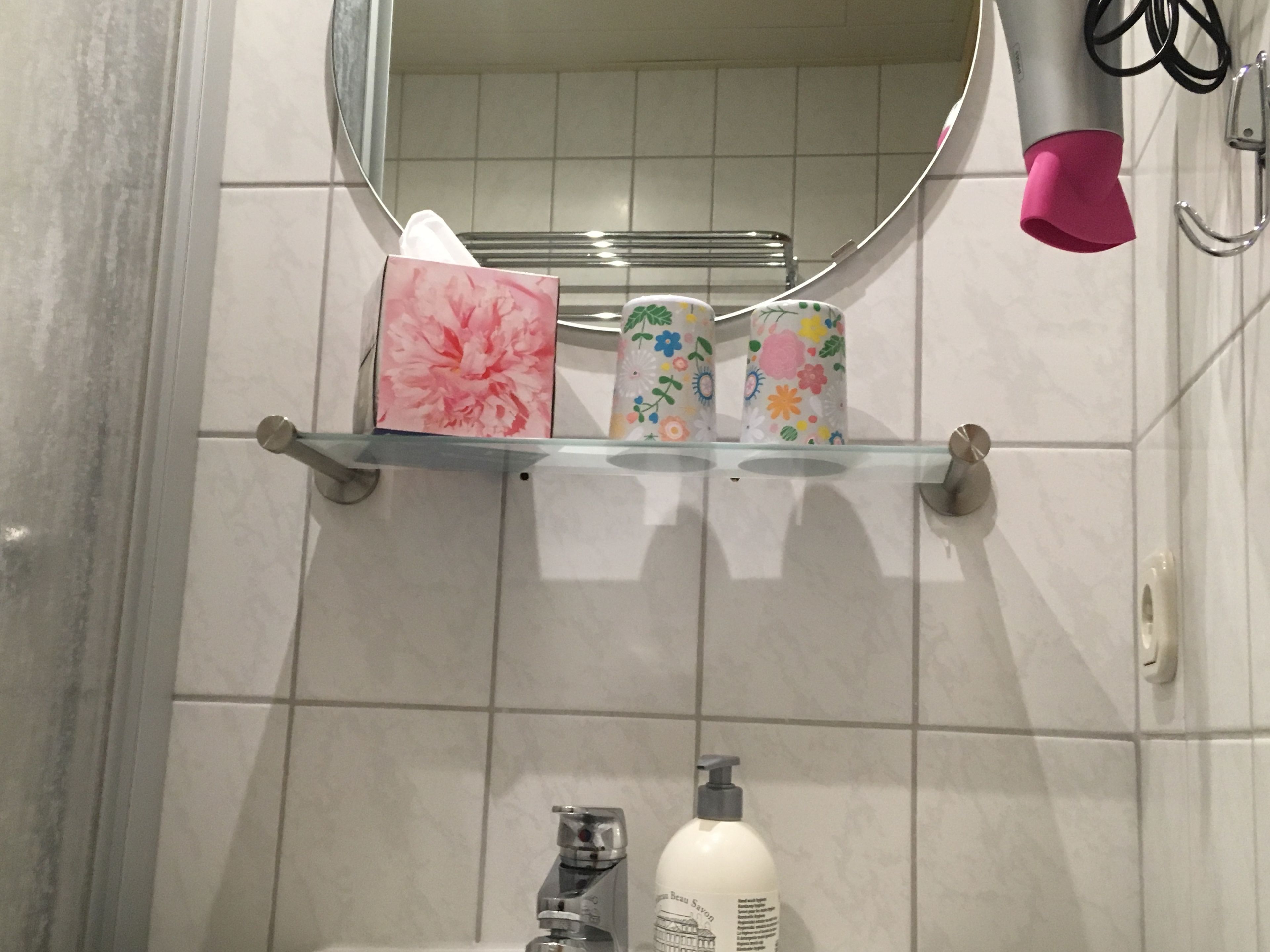 A bathroom with a mirror, a shelf with toiletries, and a hand dryer.