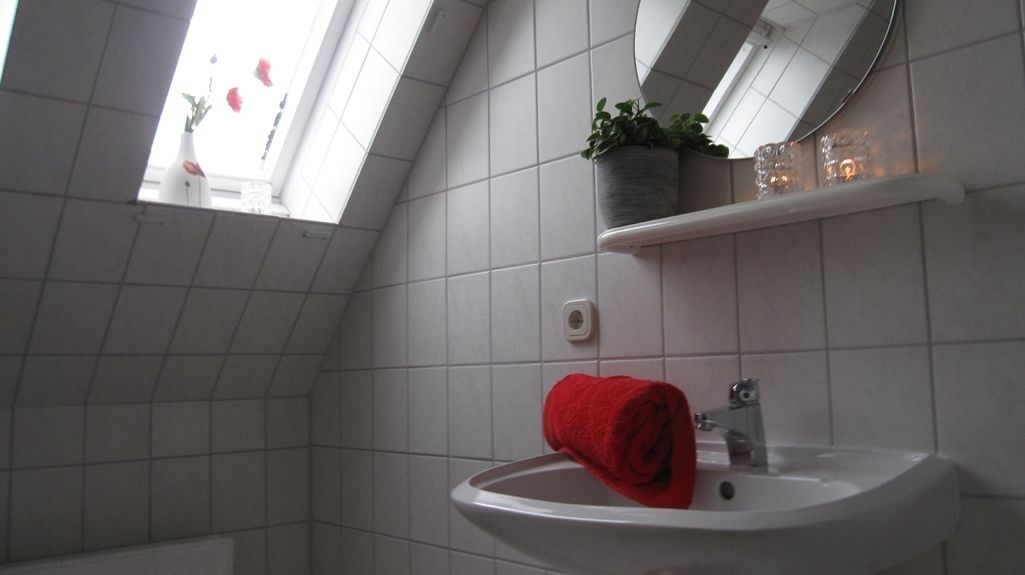 A bathroom with a skylight, white tiles, a sink, a mirror, a towel, and a potted plant.
