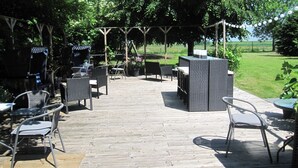 Un patio al aire libre con mobiliario de mimbre, una mesa central y una pérgola con guirnaldas de luces.