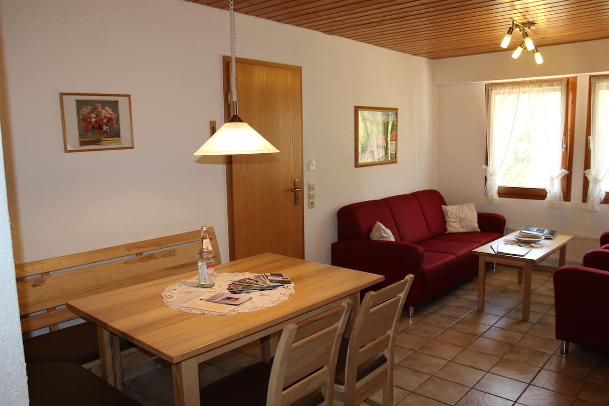 Uma sala de estar acolhedora com uma mesa de jantar de madeira, um sofá vermelho e teto de madeira.