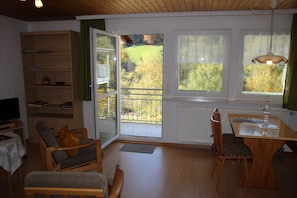 Un salon avec un plancher en bois, un canapé, une table à manger avec des chaises, une bibliothèque et un téléviseur.