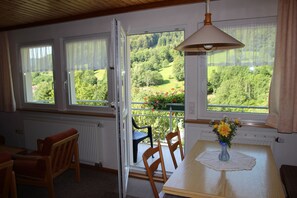 Une pièce avec une table et des chaises, un vase rempli de fleurs et une vue sur la verdure grâce à de grandes fenêtres.