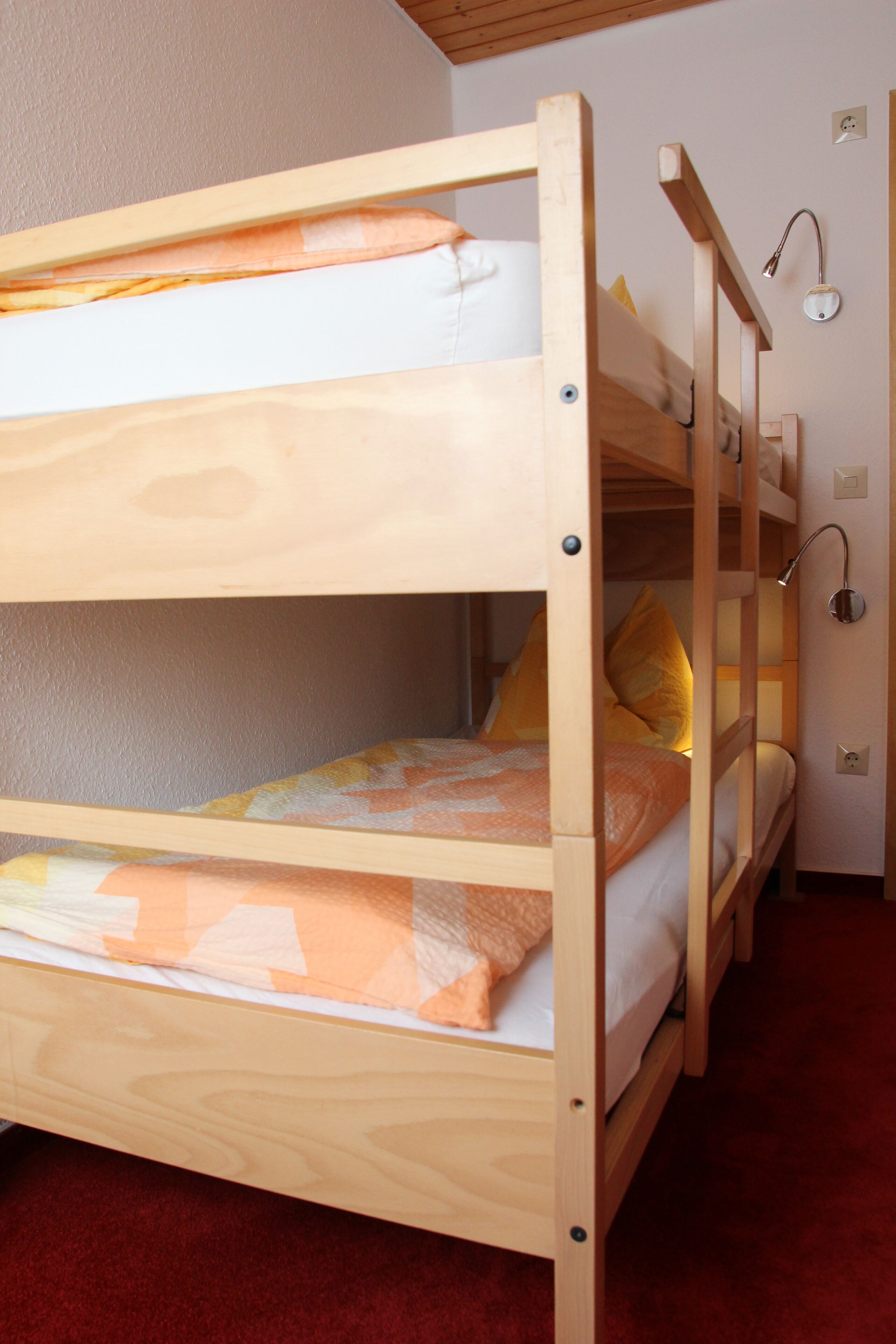 A bunk bed with two levels, a wall-mounted light fixture, and a red carpeted floor.