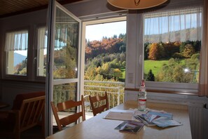 A dining area with a table, chairs, and a view of a forested landscape through large windows. - Gästehaus Steiert (Todtnau)