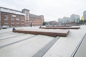 Una piazza pubblica con panchine moderne e un grande edificio in mattoni sullo sfondo.
