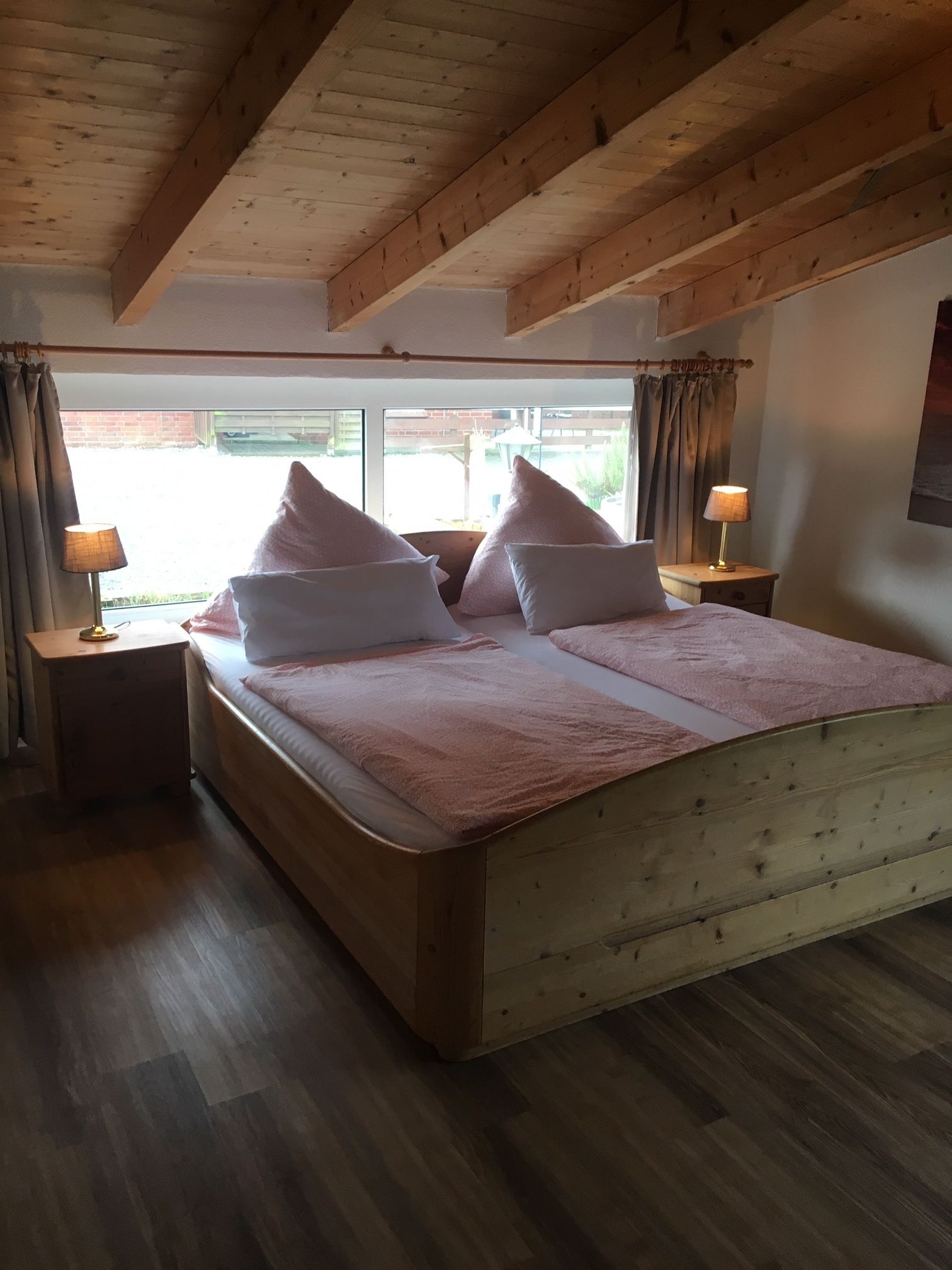 Une chambre à coucher avec un cadre en bois, un grand lit, deux tables de chevet et une fenêtre avec des rideaux.