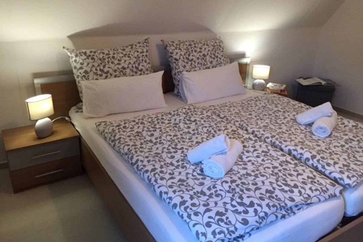 A neatly made bed with patterned bedding, two bedside lamps, and a nightstand with a lamp and a small drawer.