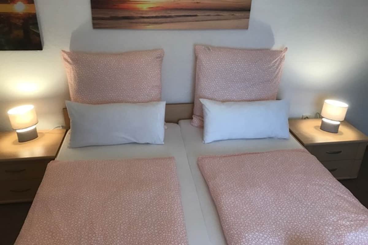 A double bed with two pillows and two bedside tables with lamps.