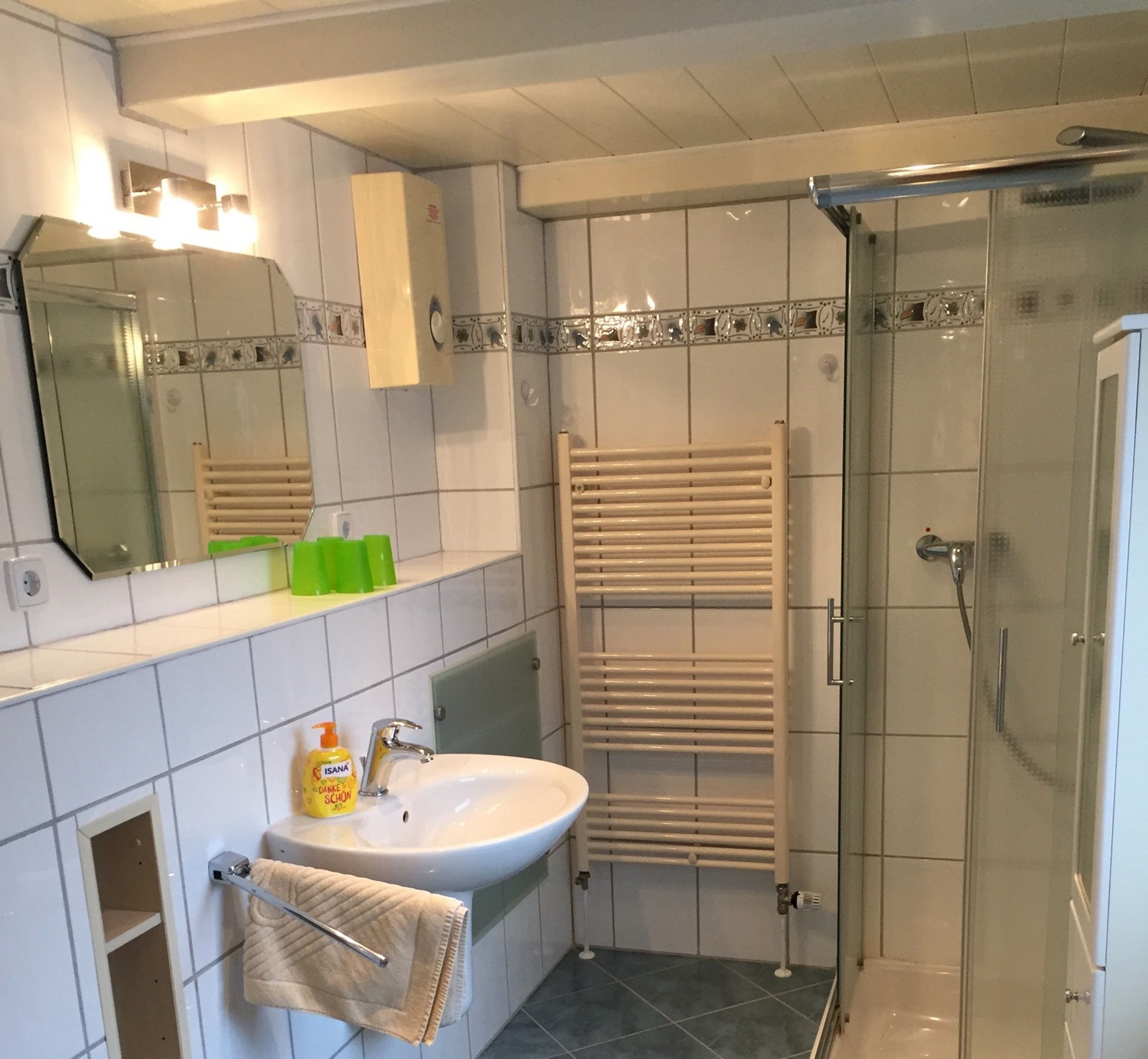 A bathroom with a sink, mirror, towel rack, shower, and tiled walls.