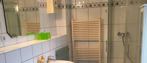 A bathroom with a sink, mirror, towel rack, shower, and tiled walls.