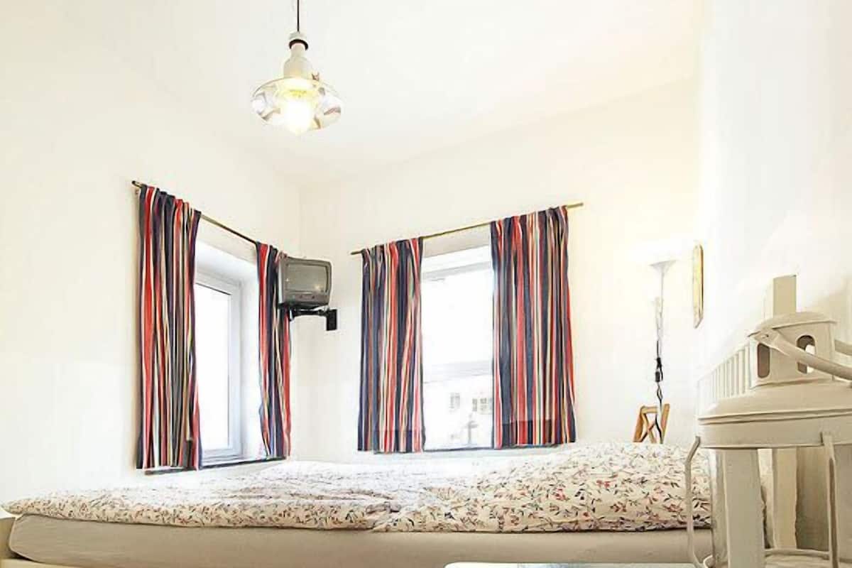 Un dormitorio con cama, televisión y ventana con cortinas a rayas.