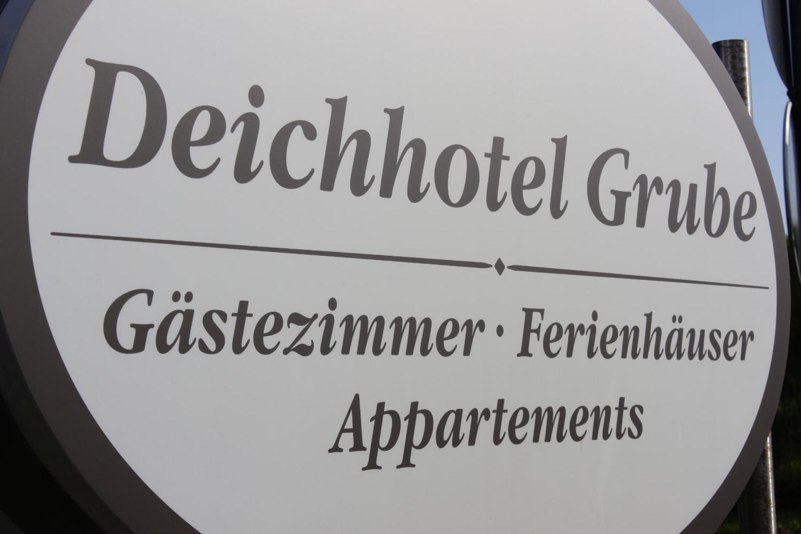 Une enseigne pour l’hôtel Deichhotel Grube avec l’inscription « Chambres d’hôtes�mi Location de maisons de vacances » indiquant la présence de chambres d’hôtes, de maisons de vacances et d’appartements.