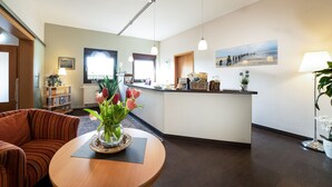 A hotel lobby with a reception desk, a round wooden table with a vase of flowers, a striped sofa, and a painting on the wall. - Deichhotel Grube (Wurster Nordseeküste)