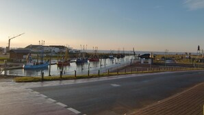 A marina with several boats docked, a road in the foreground, and buildings in the background. - Deichhotel Grube (Wurster Nordseeküste)