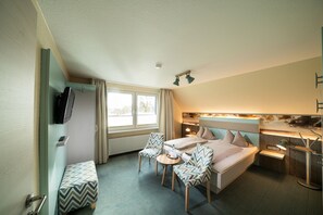 Une chambre d’hôtel comprenant un lit, deux chaises, une petite table, un téléviseur et un bureau avec une lampe.