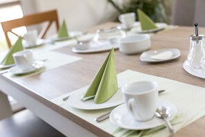 A neatly set dining table with green napkins, white plates, and cups. - Deichhotel Grube (Wurster Nordseeküste)