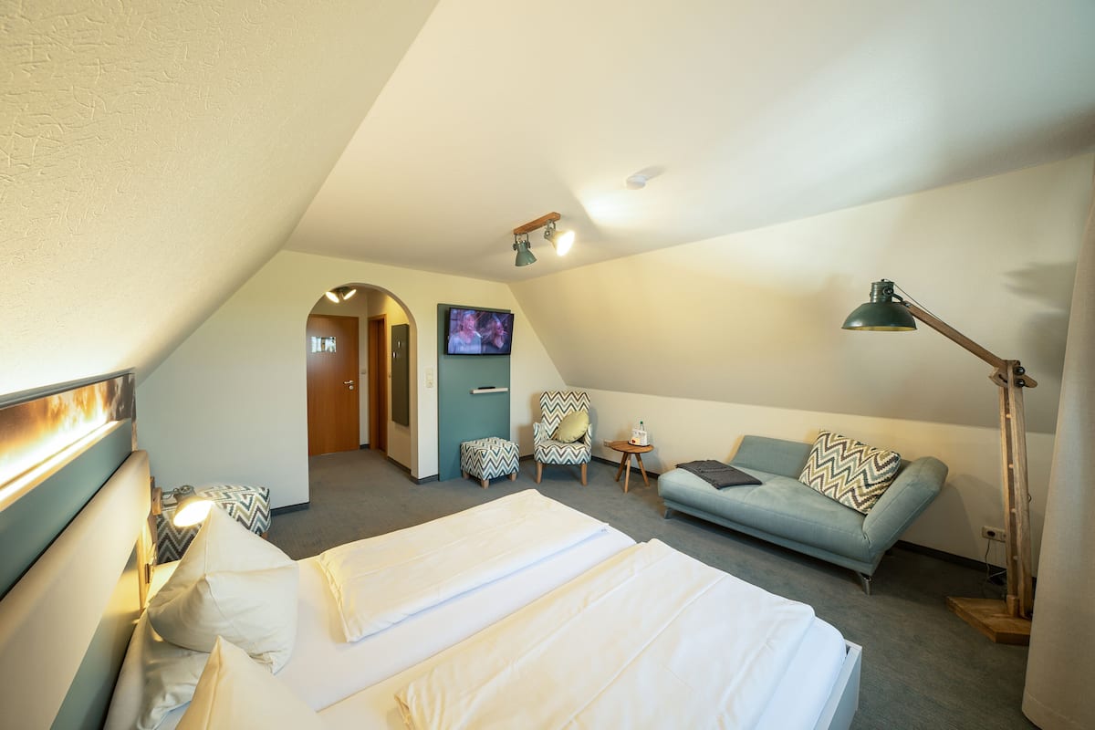 A hotel room with a bed, a sofa, a chair, a TV, and a lamp.