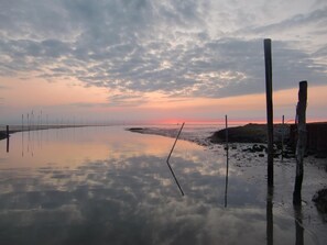 A calm beach at sunset with a clear sky, calm water reflecting the sky, and a wooden fence on the right. - Deichhotel Grube (Wurster Nordseeküste)