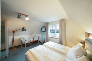 A hotel room with two beds, a desk with a chair, a television, and a window with curtains. - Deichhotel Grube (Wurster Nordseeküste)