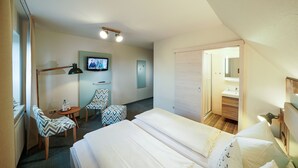A hotel room with two beds, a television, a desk with a chair, and a bathroom visible through an open door. - Deichhotel Grube (Wurster Nordseeküste)