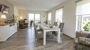A spacious living area with a dining table, comfortable seating, and a TV mounted on the wall. - Deichhotel Grube (Wurster Nordseeküste)