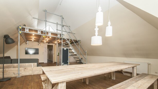 A spacious loft with high ceilings, exposed wooden beams, and a large wooden table. - Appartement 7up (Hamburg)