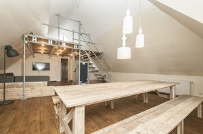 A spacious loft with high ceilings, exposed wooden beams, and a large wooden table.