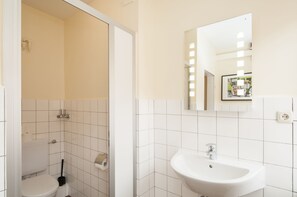 A bathroom with white tiles, a toilet, a sink, and a mirror. - Appartement 7up (Hamburg)