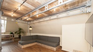 A modern room with a wooden ceiling, exposed pipes, a grey sectional sofa, a wooden bench, a potted plant, and a floor lamp. - Appartement 7up (Hamburg)
