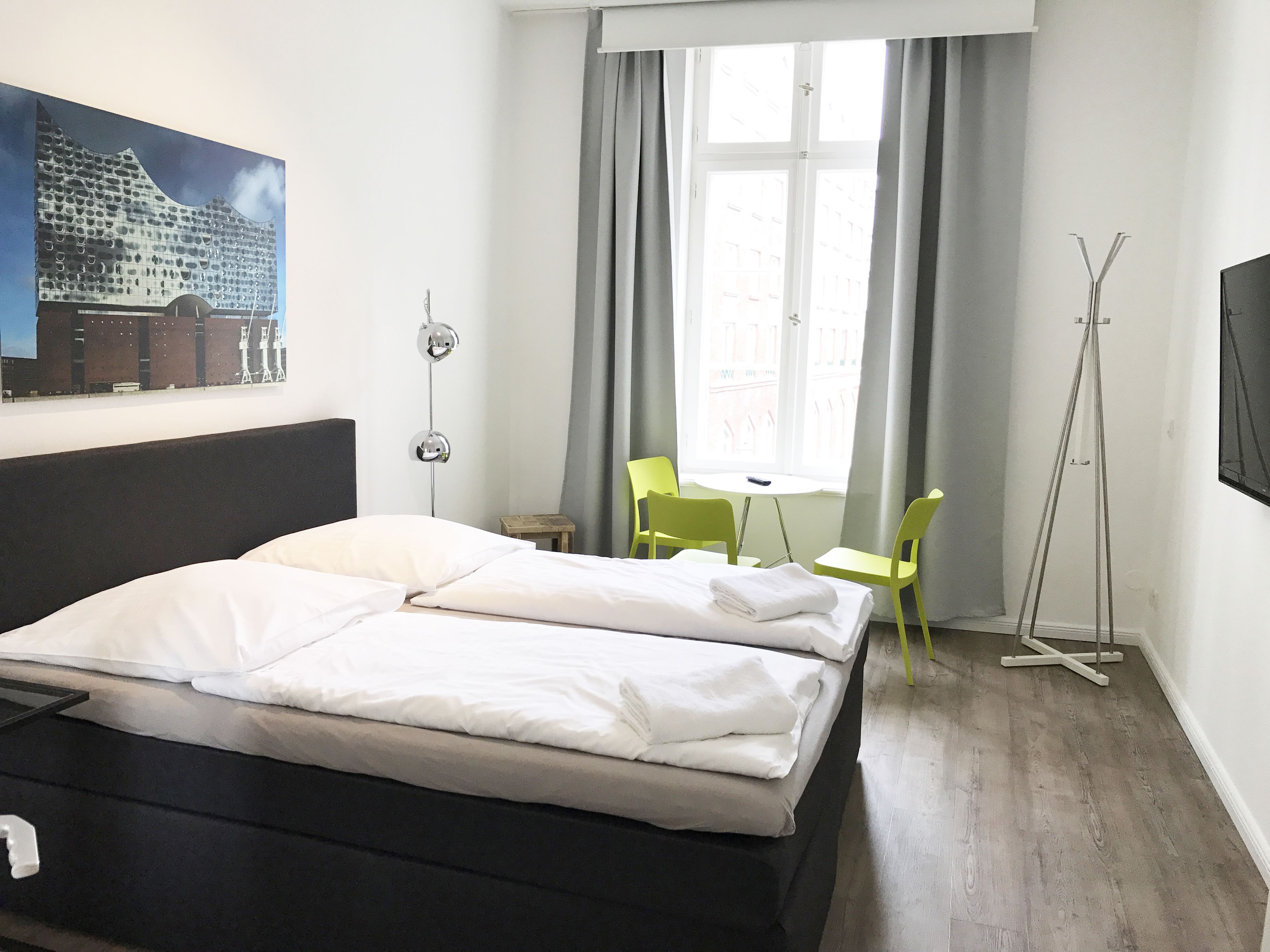 A hotel room with a bed, a desk, two chairs, a standing lamp, and a painting on the wall.