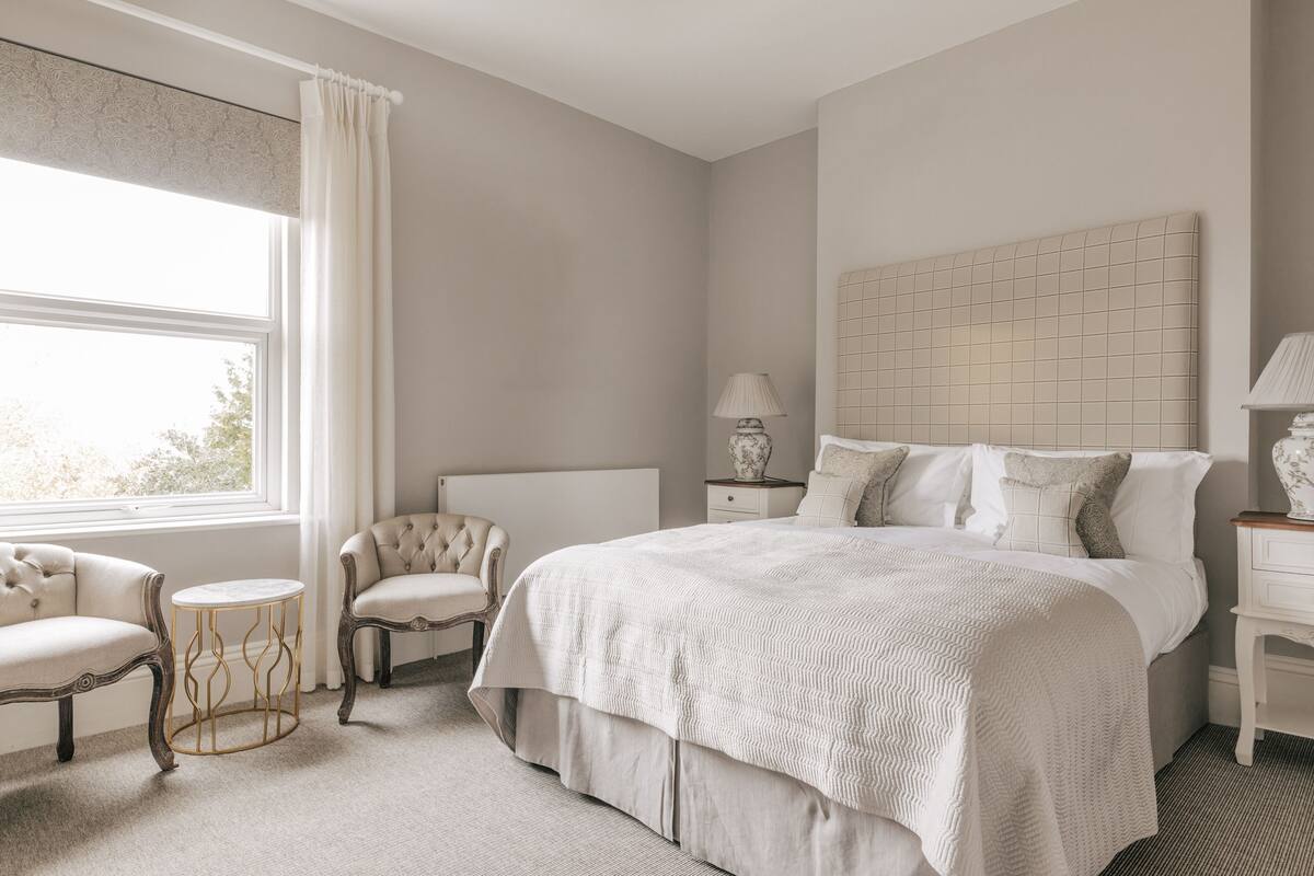 Une chambre à coucher avec un grand lit, deux fauteuils, une petite table ronde et une table de chevet avec une lampe.