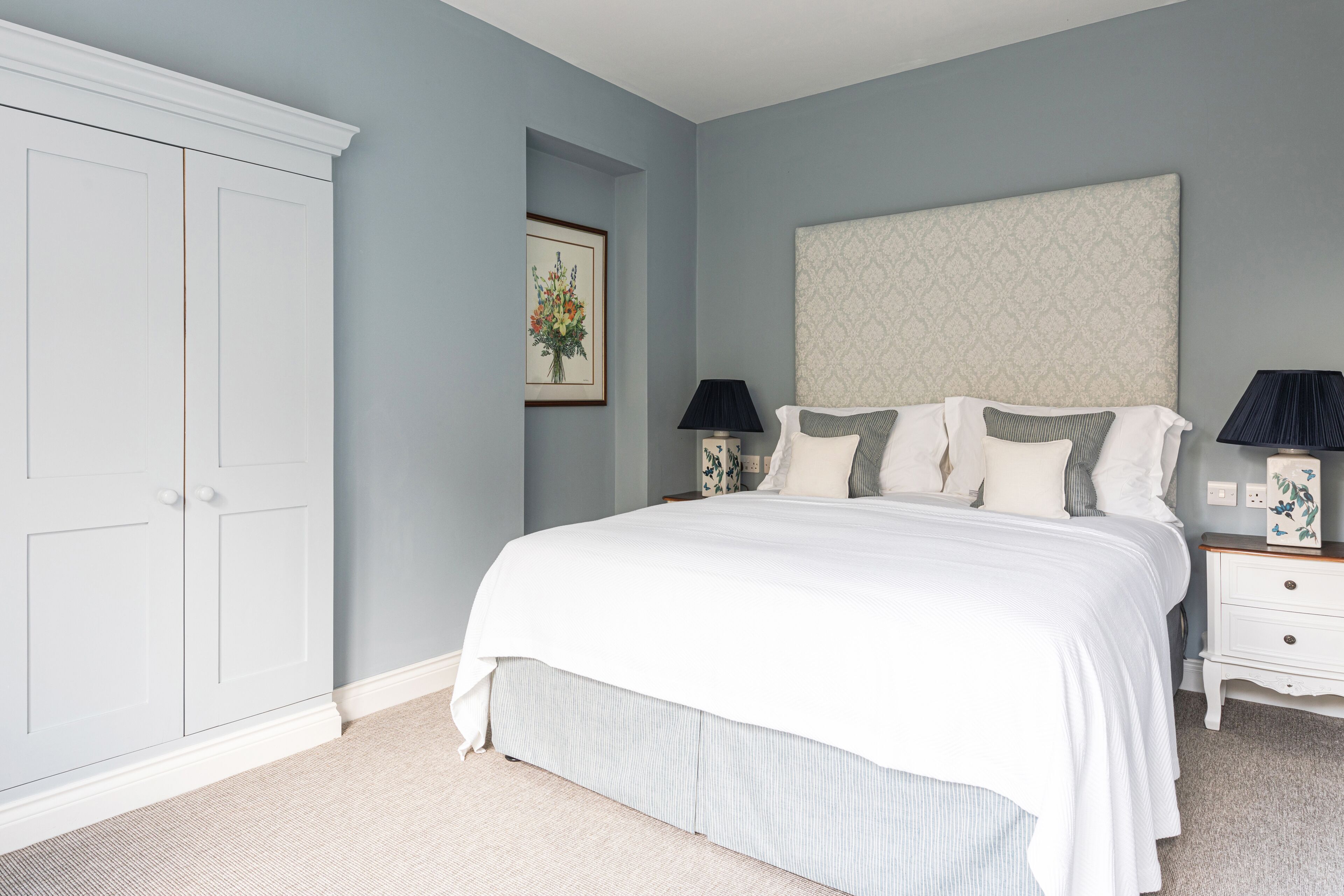 A bedroom with a large bed, a wardrobe, a nightstand with lamps, and a framed picture on the wall.