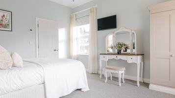 Un dormitorio con cama, tocador con espejo, cómoda y televisor en la pared.
