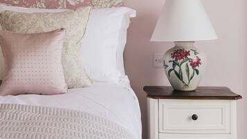 A neatly made bed with a patterned bedspread, a white nightstand with a lamp, and a floral wallpaper on the wall.