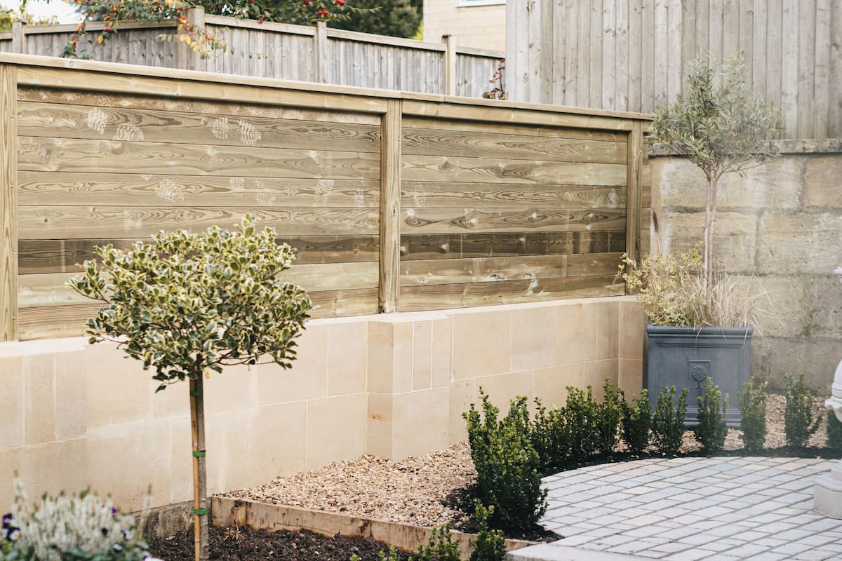 Un jardin avec une clôture en bois, un petit arbre et un jardinier planté de fleurs blanches.