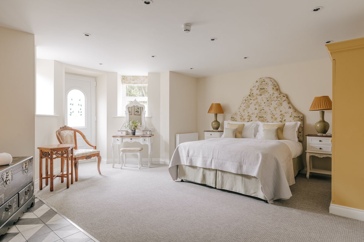 Une chambre à coucher avec un grand lit, un bureau avec une chaise, une commode et deux tables de chevet avec des lampes.