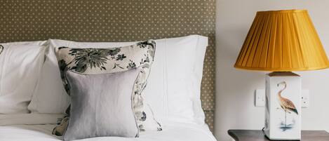 A neatly made bed with white linens and a floral pillow, a bedside table with a lamp featuring a bird design, and a polka-dotted wall.