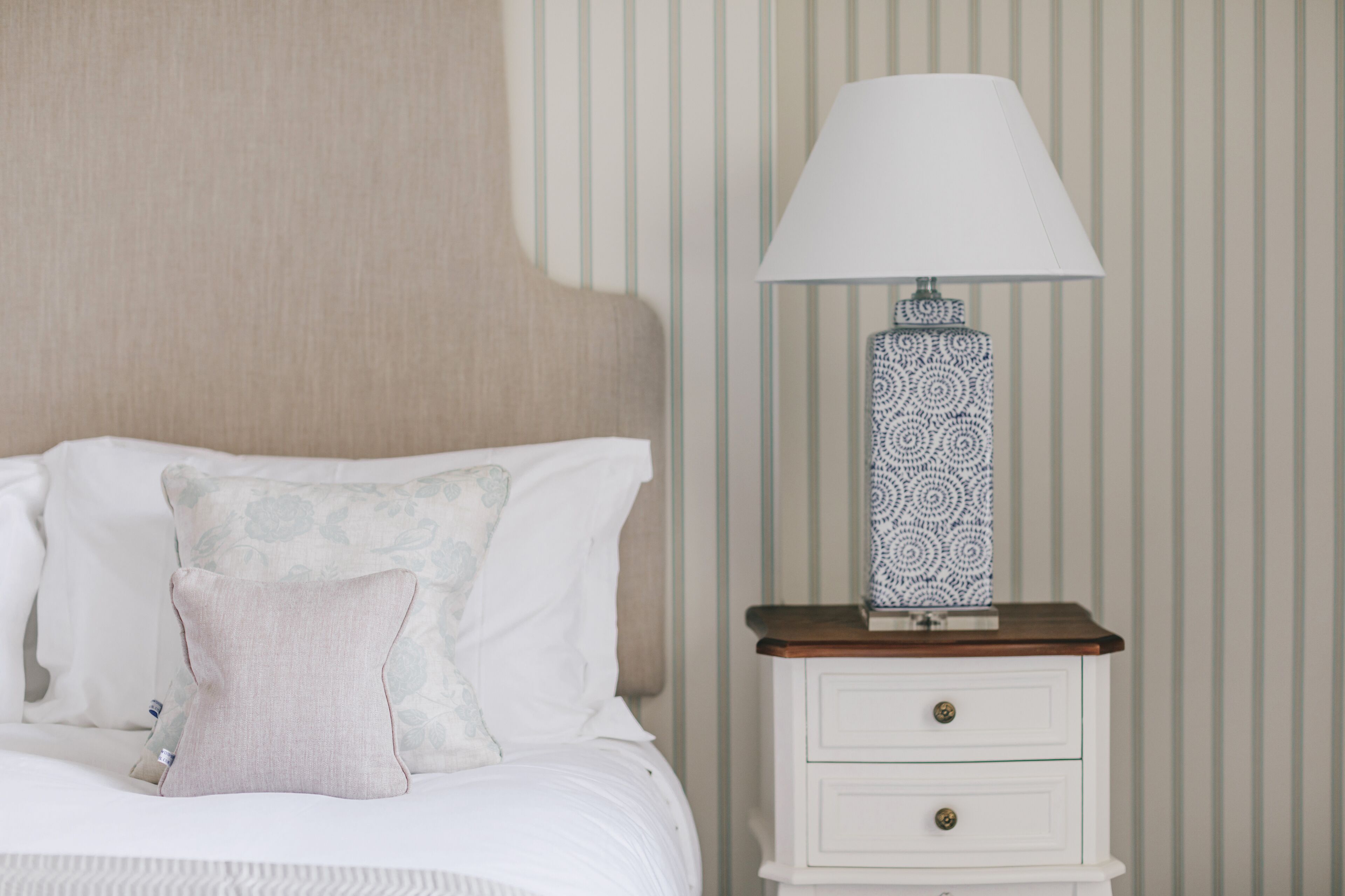 A neatly made bed with pillows, a bedside lamp, and a nightstand with drawers.