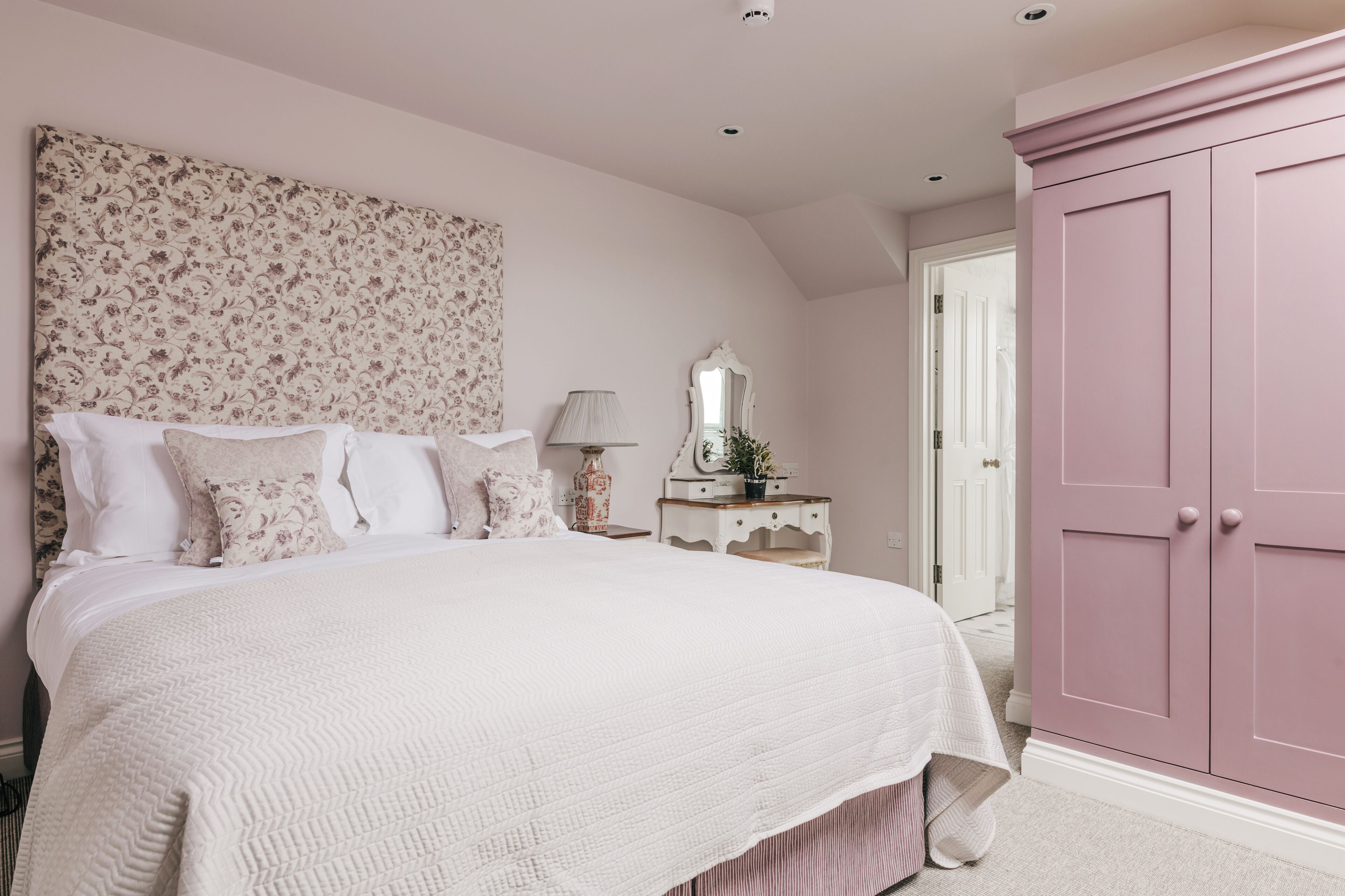 A bedroom with a large bed, a dresser, a nightstand, and a mirror.