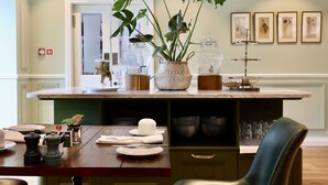 Une cuisine dotée d’un plan de travail en marbre, d’une table à manger mise avec des assiettes et des couverts, d’une machine à café et d’une plante décorative.
