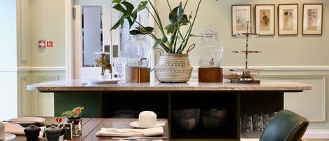 Une cuisine dotée d’un plan de travail en marbre, d’une table à manger mise avec des assiettes et des couverts, d’une machine à café et d’une plante décorative.