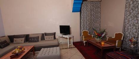 A living room with a sofa, ottoman, coffee table, TV, and a dining area with chairs and a table.