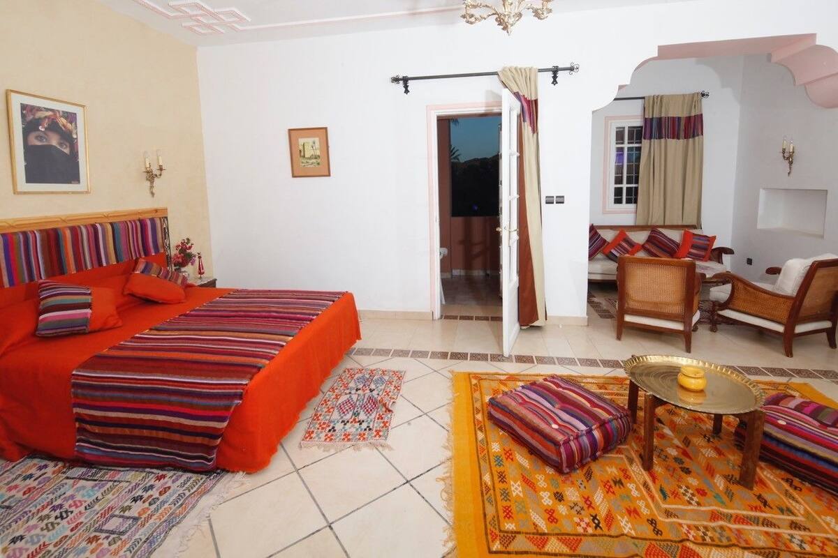 Une chambre à coucher avec un lit, un canapé, une petite table et une chaise. Une porte donne accès à une autre pièce.