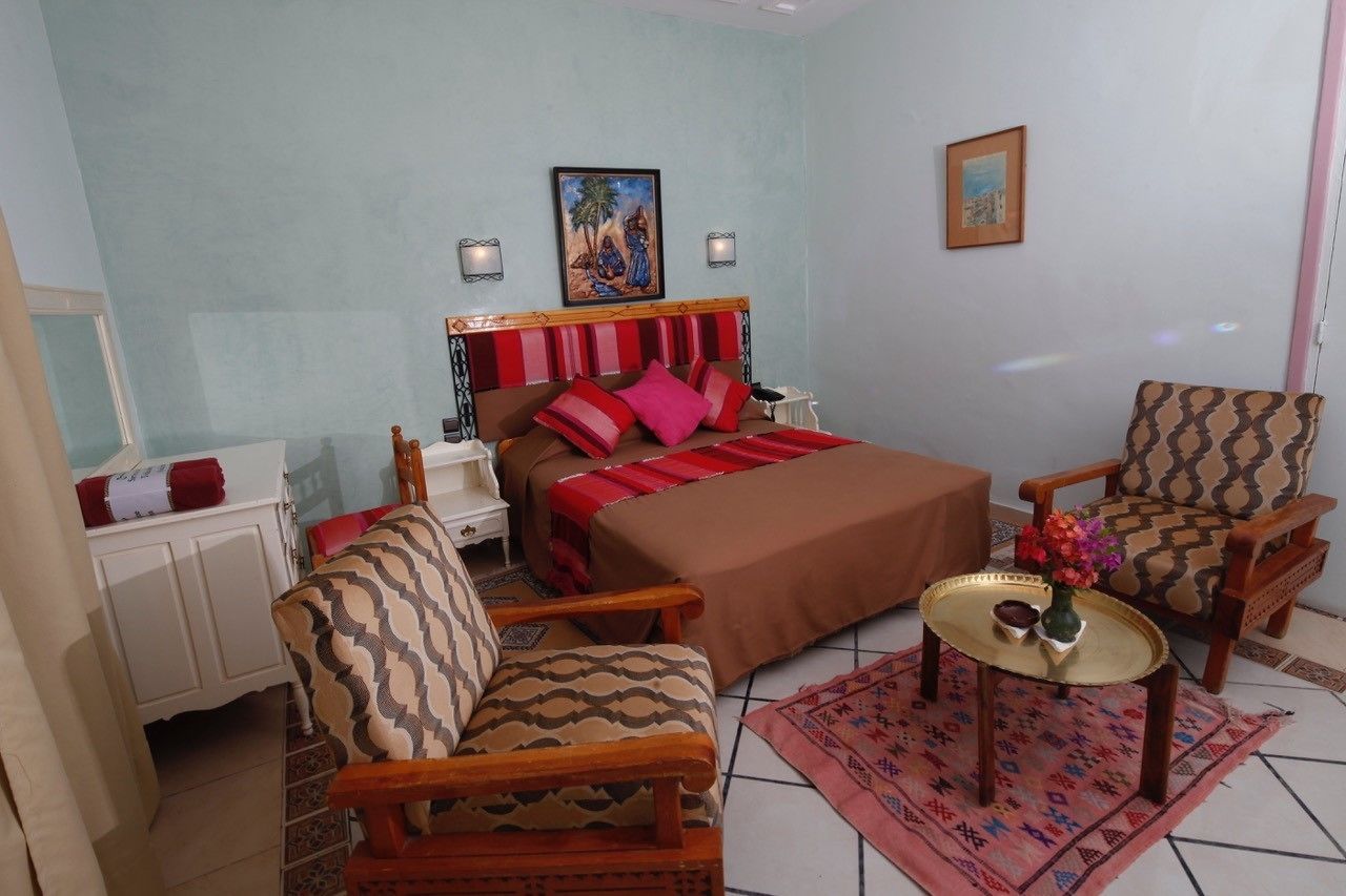 Un dormitorio con cama, dos sillas, una mesita con un florero y una mesita de noche.