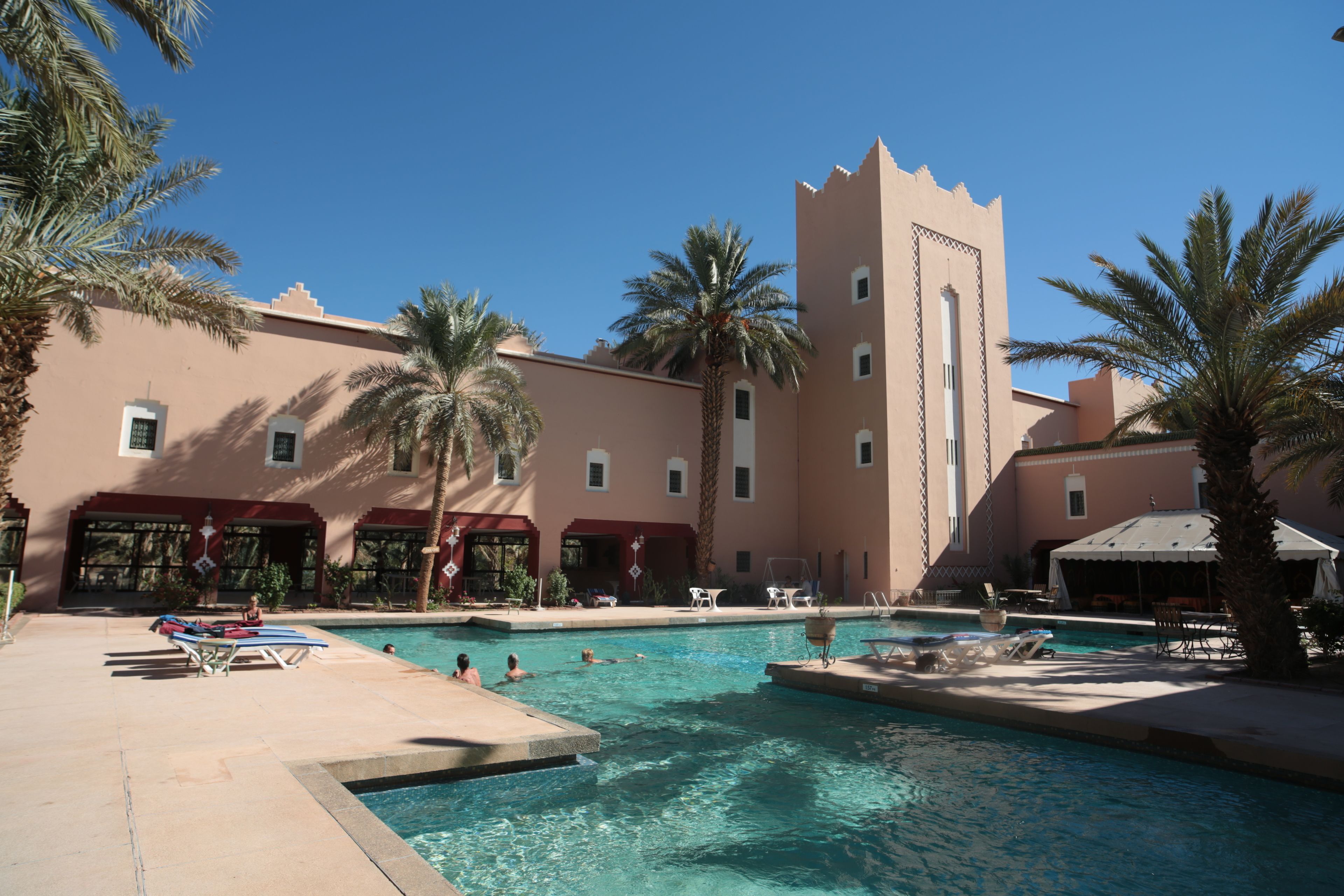 A pool area with multiple swimming pools, palm trees, and a building with a unique architectural design.