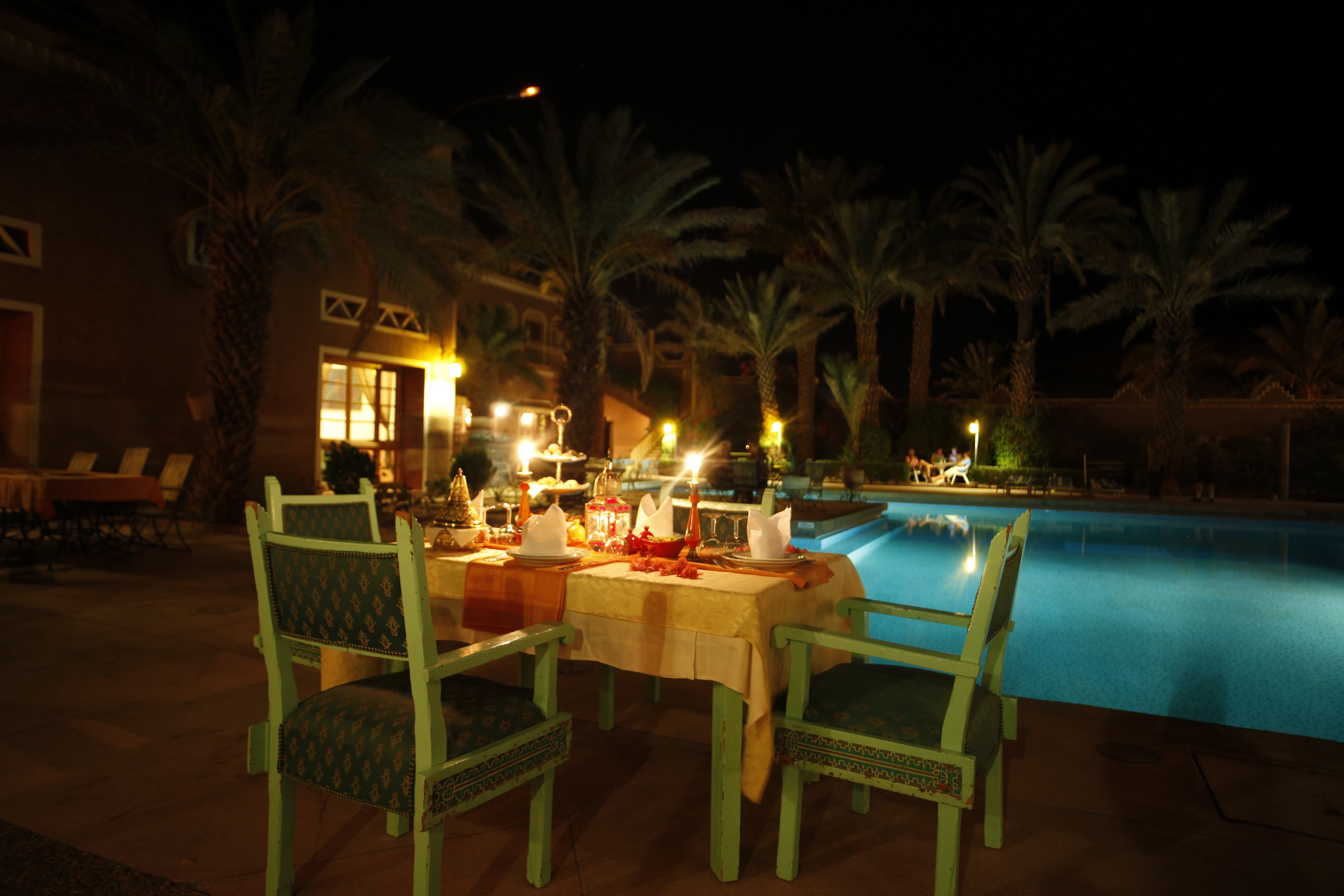 An outdoor dining area with a pool, green chairs, and a table set for a meal.