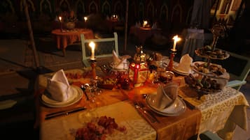 A dimly lit dining area with tables set for a meal, candles, and a variety of dishes.