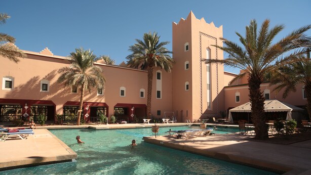 Zona de piscina con agua cristalina, palmeras y un edificio con torre.