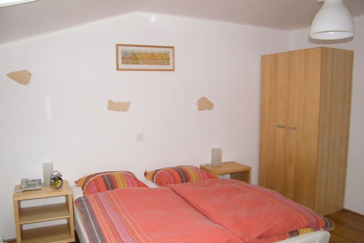 A bedroom with a bed, two bedside tables, a wardrobe, and a framed picture on the wall.
